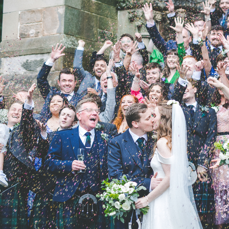 Cottiers Weddings — Bride and groom kissing outside of the venue with guests and confetti